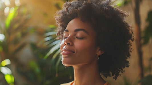 Beautiful black woman standing in front of plants with her eyes closed as she meditates.