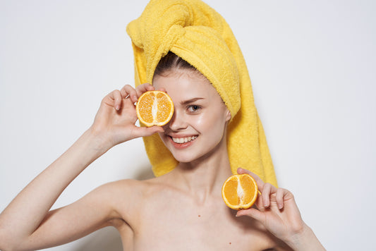 Cheerful woman with oranges in her hand and glowing skin with a yellow towel on her head.